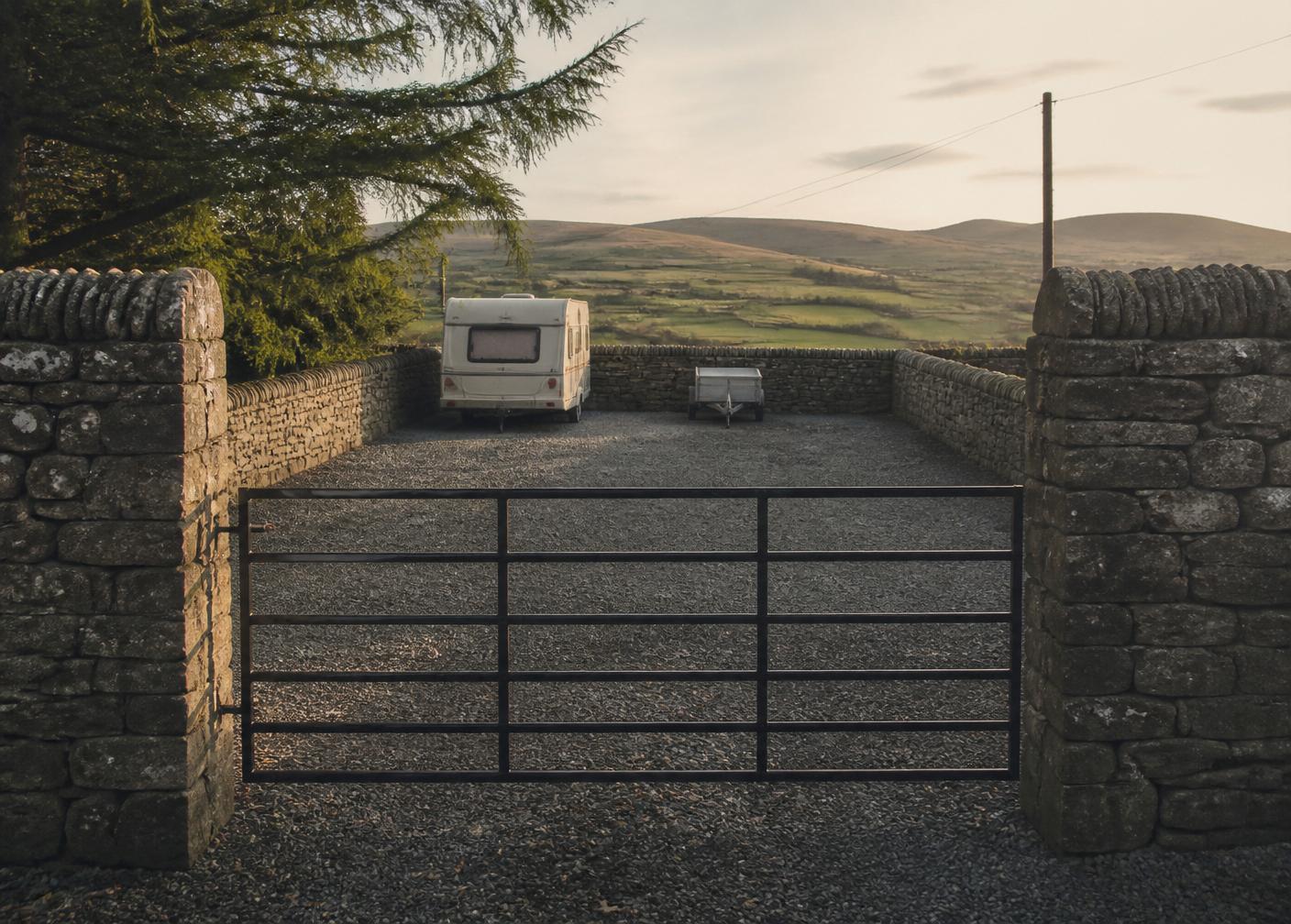 Secure gravel yard behind a dry stone wall with a caravan parked at the far end